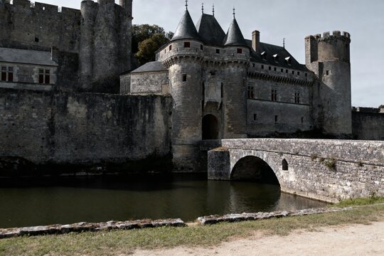 Medieval stone castle with moat and arched bridge, featuring towers and fortified walls