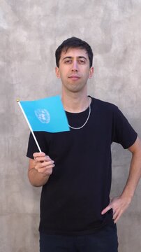 Vertical shot of a man waving United Nations flag in slow motion. United Nations organization flag.