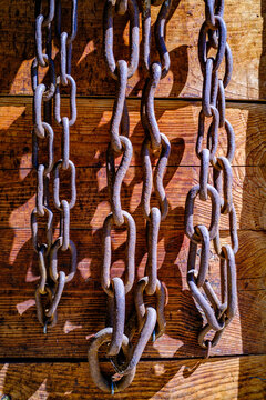 Close view of metal chains hanging against wooden surface in a workshop setting during daytime with natural light