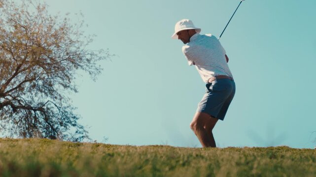 Golfer hits 3 wood over camera in extreme slow motion on sunny summer day wearing bucket hat, 4k 800fps slowmo golf shot low angle pod