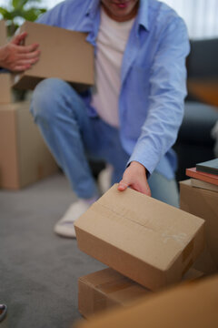 Young Asian man unpacking cardboard boxes on living room sofa during home relocation move
