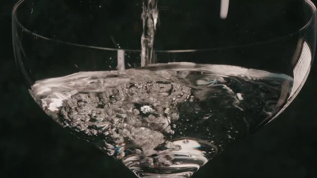 Pouring clear liquid over martini glass close up