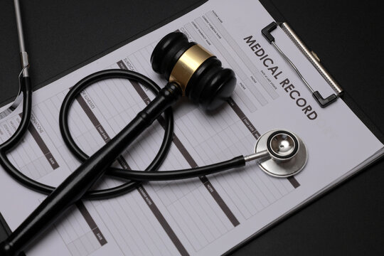 Serious medical documentation system representation featuring black stethoscope with legal wooden gavel on clipboard record paper