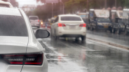 Fototapeta premium Abstract rainy day perspective from behind a white car as it drives on a wet city road. Scene captures the movement of traffic and the reflective glistening surfaces of the wet asphalt.