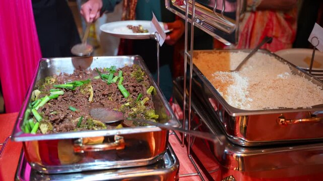 Variety catering station featuring seasoned beef with vegetables and steamed white rice served in stainless steel chafing dishes.