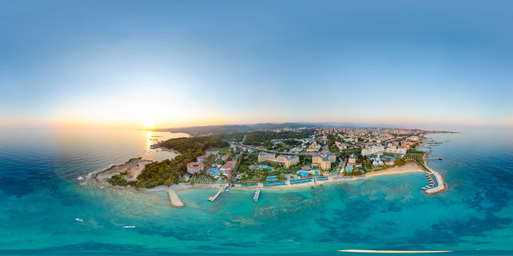Avsallar, Alanya, Turkey. 360-degree spherical panorama over a turquoise lagoon with golden sandy beaches, beachfront hotels and pine-forested hills at golden hour, aerial view
