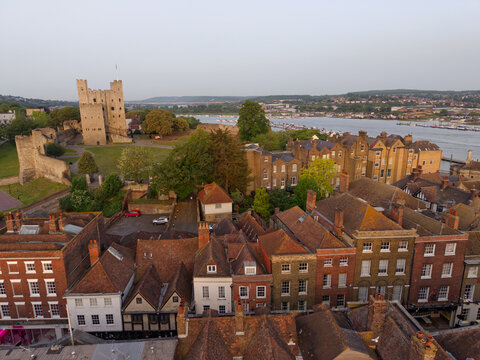 Beautiful Rochester old town at sunrise in Kent, UK. Aerial closeup view above High street with old brick buildings and tile roofs. View towards medieval stone castle and river Medway at golden hour.