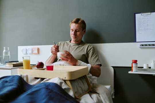 Young adult Caucasian man recovering in military hospital bed, eating meal during treatment and convalescence. Useful for veteran healthcare, patient recovery, medical support campaigns