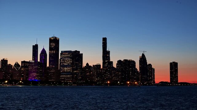 Chicago skyline at blue hour viewed across Lake Michigan, featuring illuminated downtown skyscrapers reflected against a deep blue evening sky.