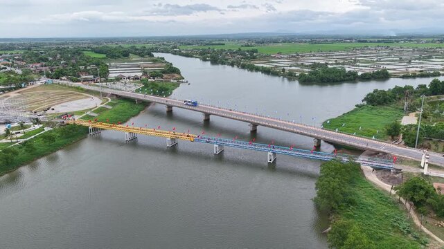 Aerial drone shot captures the historic Hien Luong Bridge stretching across the Ben Hai River at the former demilitarized zone, with colorful flags decorating the bridge.