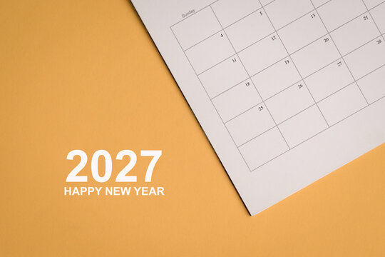 2027 Happy New Year, message next to calendar or planner, on yellow surface.