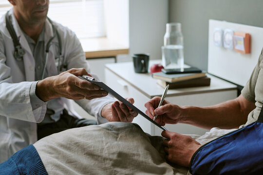 Unrecognizable man with arm imjury signing medical document during consultation with doctor in military hospital, supporting treatment consent and healthcare communication for medical marketing