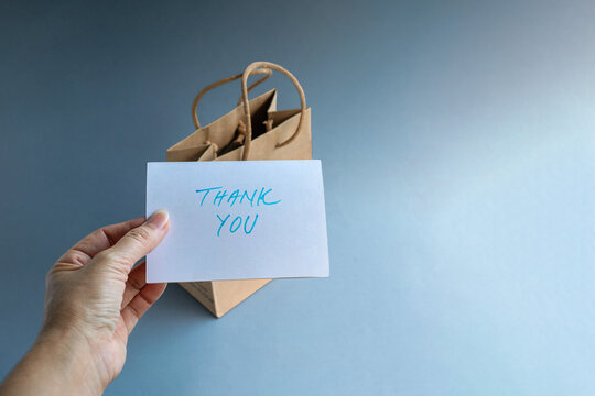Hand holding a thank you card with a gift bag in the background.