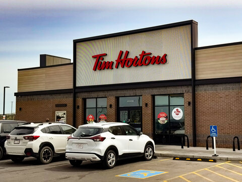 Calgary, Canada - 06 15 2026: Fast food restaurant exterior featuring a modern building Tim Hortons design with large windows and a prominent sign, surrounded by parked vehicles in a parking lot