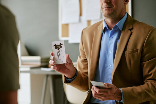 Medium shot of middle aged Caucasian man holding inkblot cards and conducting psychological assessment in clinical setting. Useful for mental health therapy, diagnosis, counseling marketing