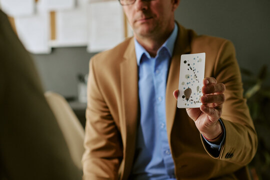 Middle aged Caucasian man holding up inkblot card during psychological assessment, supporting mental health diagnosis and therapy communication for clinics and counseling