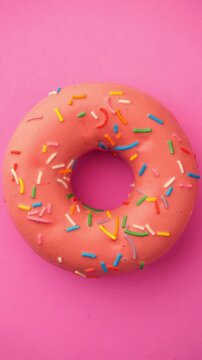 Rotating Glazed Donut with Sprinkles. Colorful donut turns smoothly on a pink background in a seamless loop.