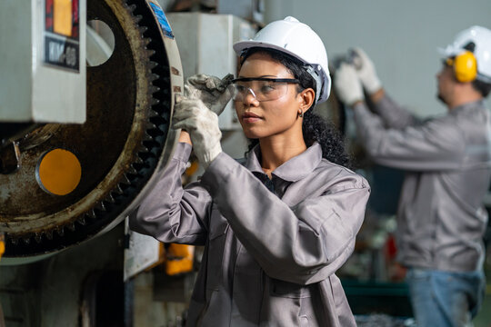 young black female conducting a routine quality control and safety inspection heavy machinery, professional diverse technician working on machine maintenance in industrial plant