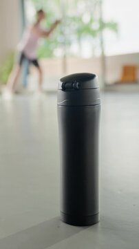 Vertical video of young adult Caucasian woman picking up black thermos, drinking water, and returning to workout. Ideal for sports nutrition and healthy lifestyle advertising