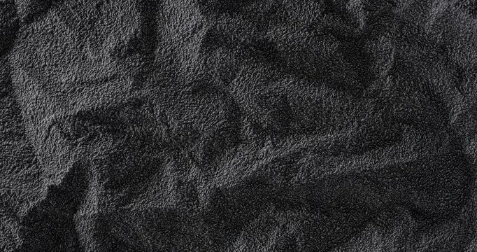 Rotating Dark Granular Texture. A rough black surface rotates smoothly under a directed soft beam of light, revealing its raised relief.