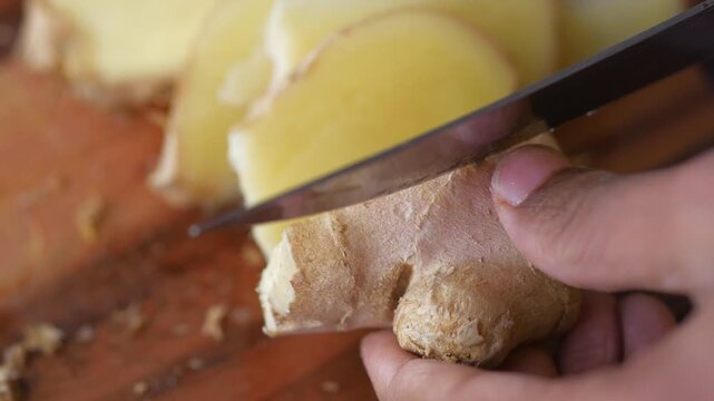 Close up of sharp knife slicing fresh organic ginger root on wooden cutting board with dynamic motion