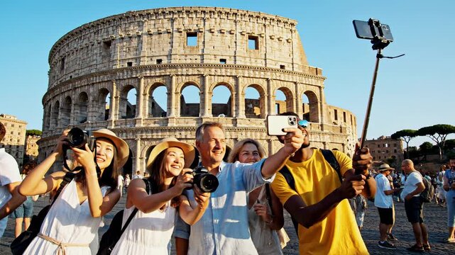 A diverse group of cheerful travelers captures memories together using cameras and phones while visiting the famous ancient Colosseum amphitheater located in the historic city center of Rome
