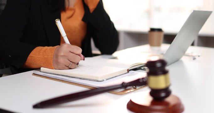 Young asian woman lawyer managing her legal work, talking on a mobile phone and writing important details in a notebook, symbolizing dedicated professional service and communication