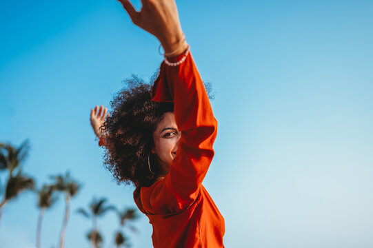 Beautiful woman joyfully raises her arms high celebrating life against a vibrant tropical background