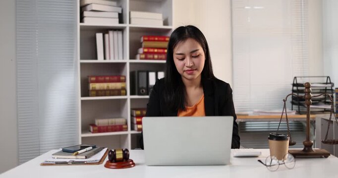 Female lawyer working on laptop, researching cases and legal documents in a law office or firm, representing justice and legal assistance concepts