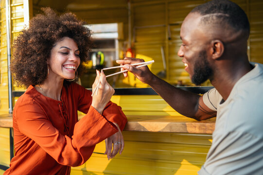 Happy black couple traveling and enjoying exotic street food with chopsticks, having fun