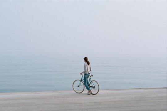 Woman with bicycle walks along foggy sea