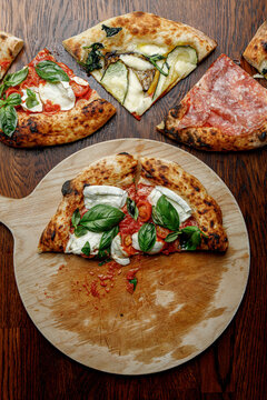 Half of a finished pizza next to slices of other pizzas.