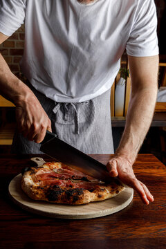 A pizzaiolo cuts a freshly made pizza with a knife. Isolated
