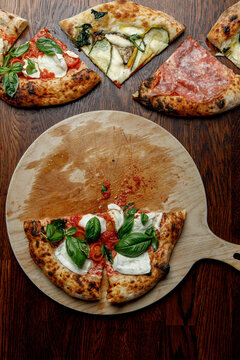 Half of a finished pizza next to slices of other pizzas.