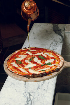 A pizzaiolo drizzles oil over a freshly baked Margherita pizza.
