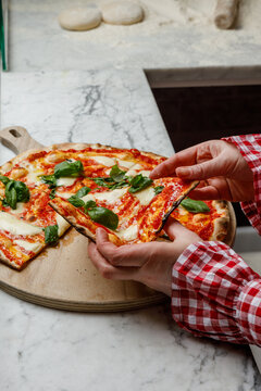 A young woman takes a slice of freshly baked pizza.