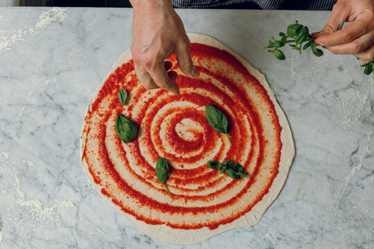 A pizzaiolo places cheese and basil onto a pizza base. Isolated.
