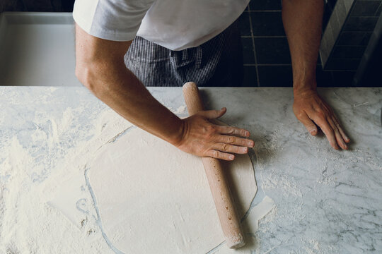 A pizzaiolo rolls out dough for artisanal pizza. Isolated.