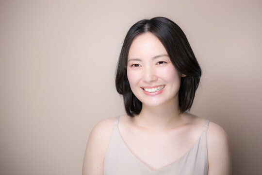 ピンクベージュ背景笑顔の美しい日本人女性　美しい素肌とナチュラルメイクの美容見上げる笑顔のクローズアップポートレート　幸せや多幸感のイメージ