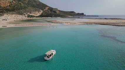 Horizontal aerial view of a small white pleasure boat anchored in the crystal clear turquoise water of Balos lagoon on the island of Crete in Greece © moryachka