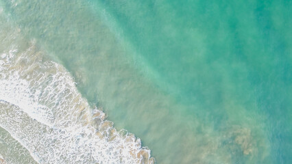 Horizontal top down aerial view of crystal clear turquoise sea water washing onto a sandy beach with soft white foam creating a beautiful minimalist texture © moryachka
