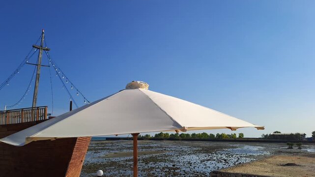 Aesthetic beach cafe seating with umbrella moving in hot windy heatwave by the sea, perfect summer holiday background, relaxing vacation vibe, canicule and tropical seaside concept