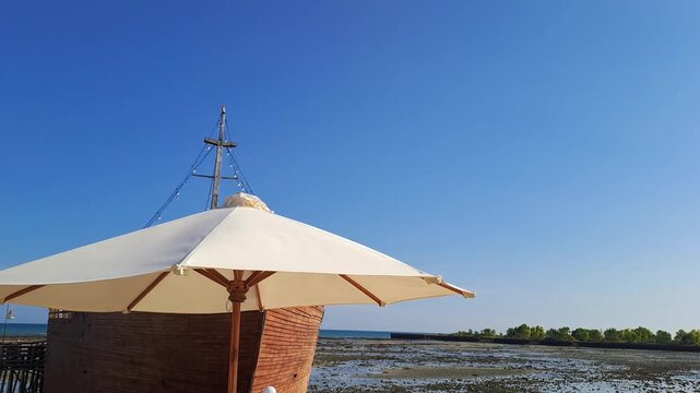 Aesthetic beach cafe seating with umbrella moving in hot windy heatwave by the sea, perfect summer holiday background, relaxing vacation vibe, canicule and tropical seaside concept