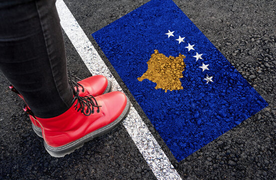 a woman with a boots standing on asphalt next to flag of Kosovo and border
