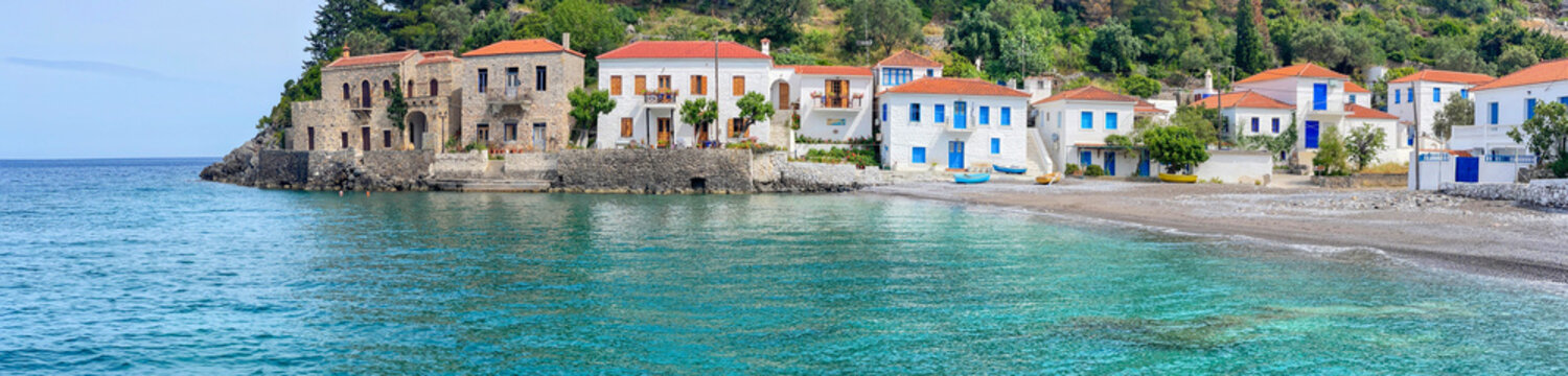 greek village at the edge of  beautiful clear blue water of the sea with white house  in front of green hill  in Peloponnese Greece