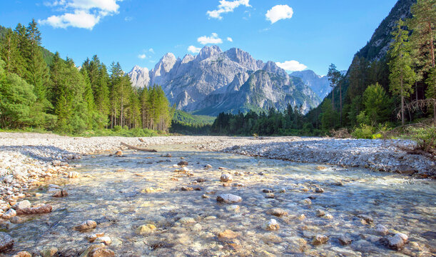 river bed with little water and rocky peak mountains background with hills covered with forest  in italian Dolomites in Malborghetto-Valbruna, Udine province, Italy