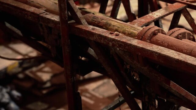 A collection of rusty metal and wooden parts is seen in an old workshop. Tools and machinery clutter the space, showing signs of wear. Dust is visible in the light coming through a window.