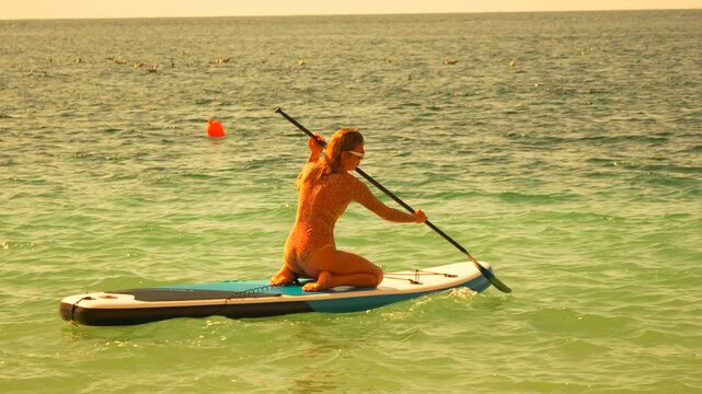 Paddleboarding woman ocean exercising on inflatable stand up board during sunny summer vacation trip