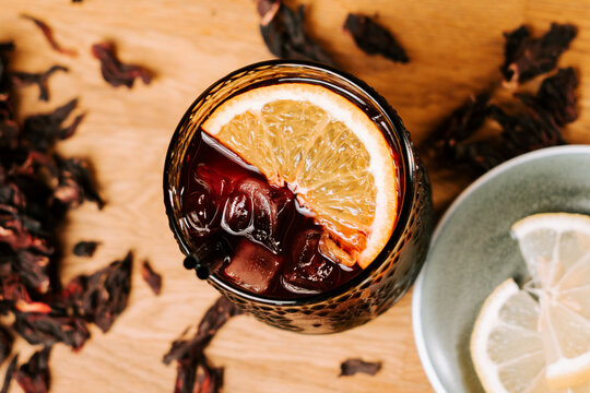 Hibiscus tea served with ice and orange slices on a wooden table during the bright afternoon hours
