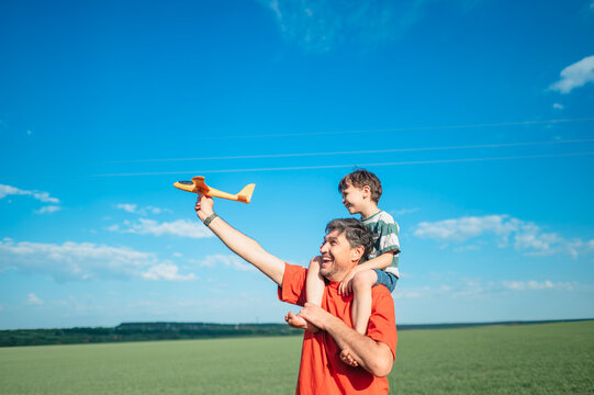 Father carries his son playing with a toy airplane outdoors